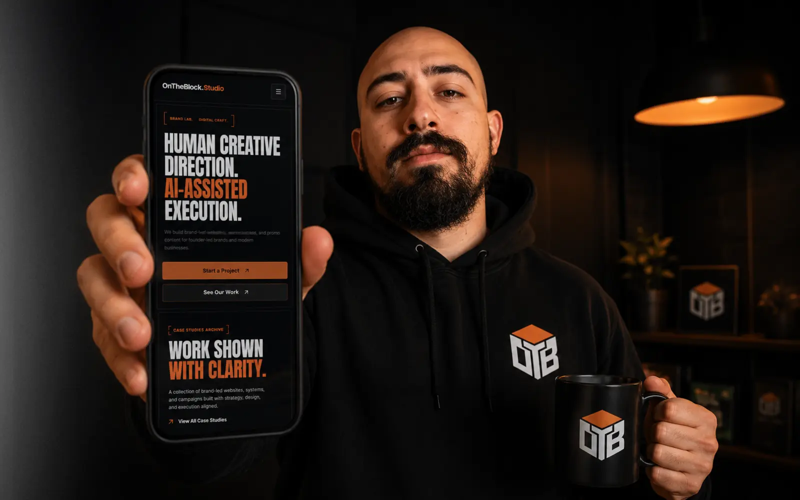 OnTheBlock Studio founder presenting the studio website on a phone while holding a branded coffee mug